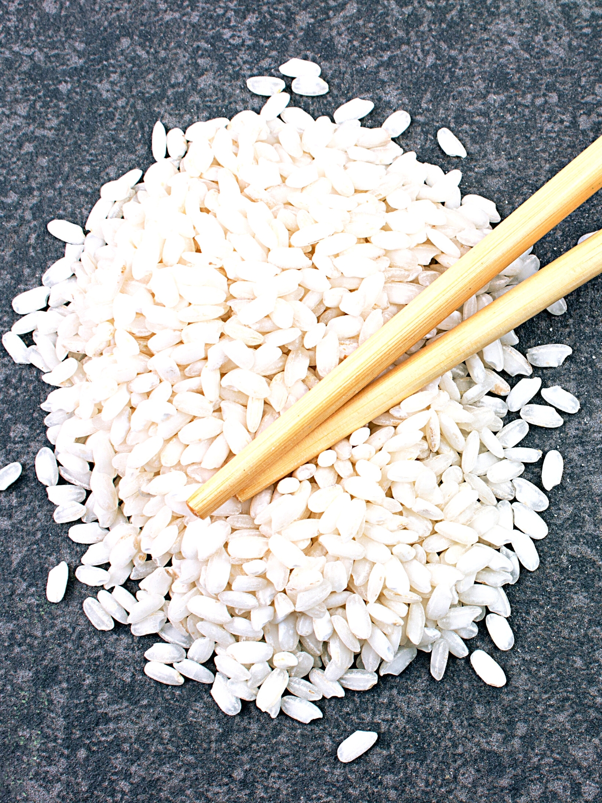 Raw Sushi Rice on a grey background with chopsticks placed on top. 