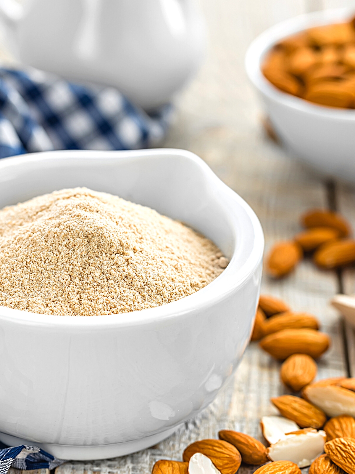 Almond flour in a white ceramic bowl and fresh almonds around it.