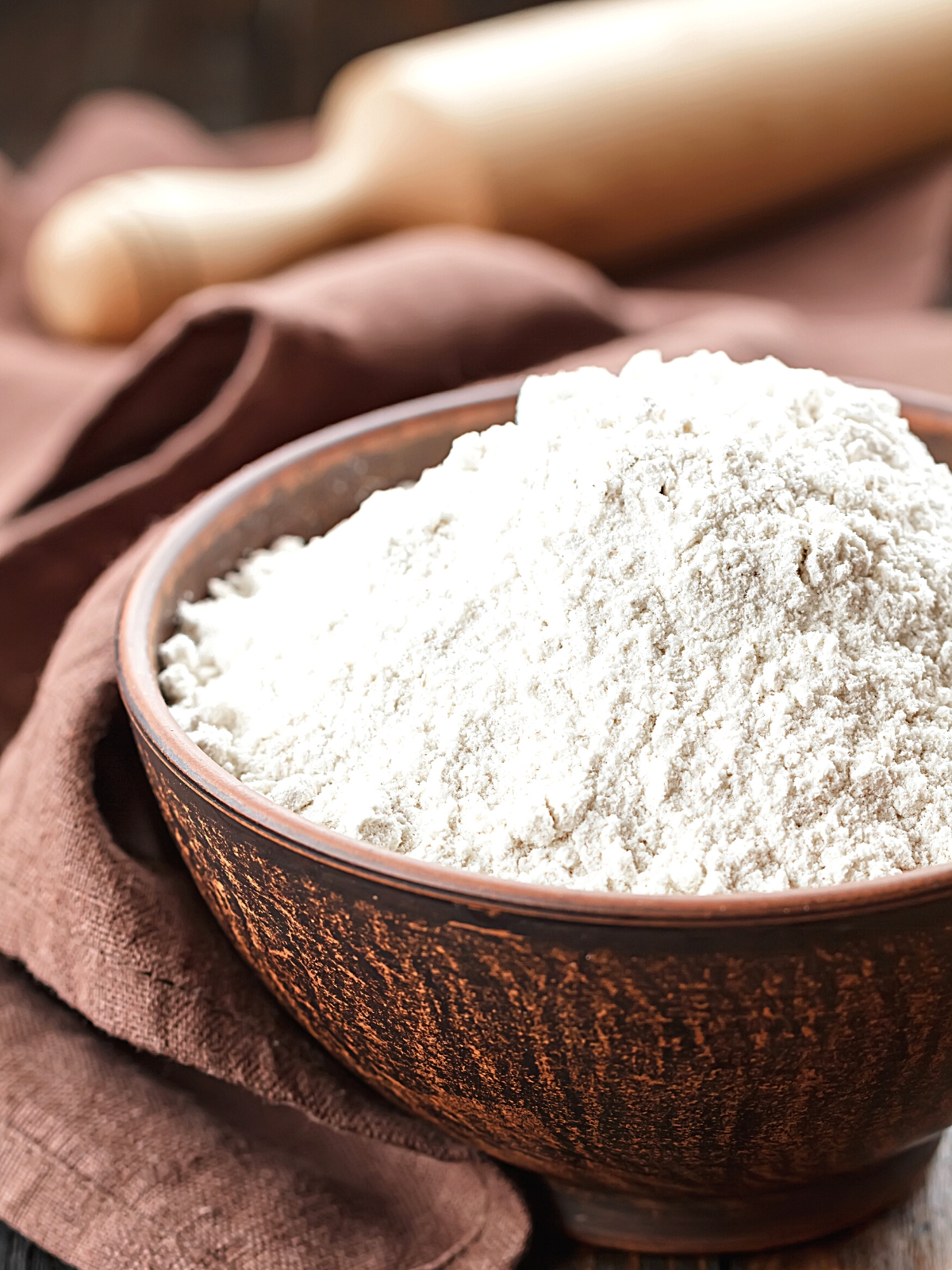 Brown Rice Flour in a wooden bowl and a rolling pin in the background.