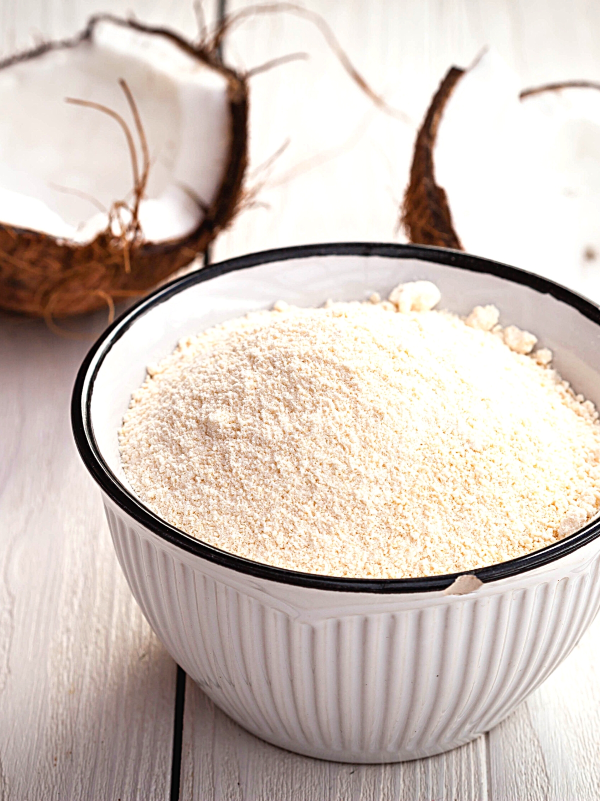 A bowl of Coconut flour with half broken fresh coconut in the background.