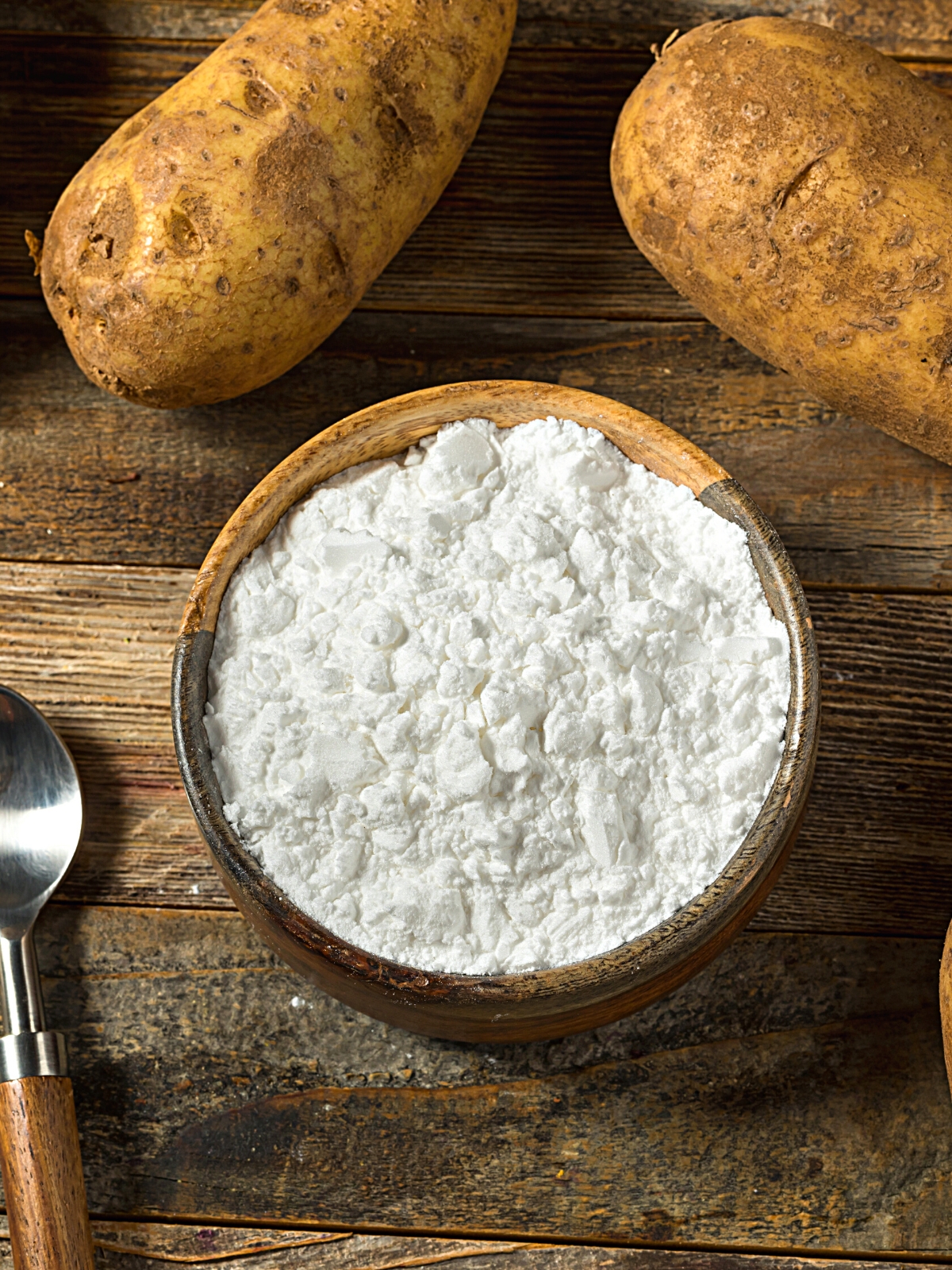 A bowl of Potato Starch, with two raw potatoes on the side.