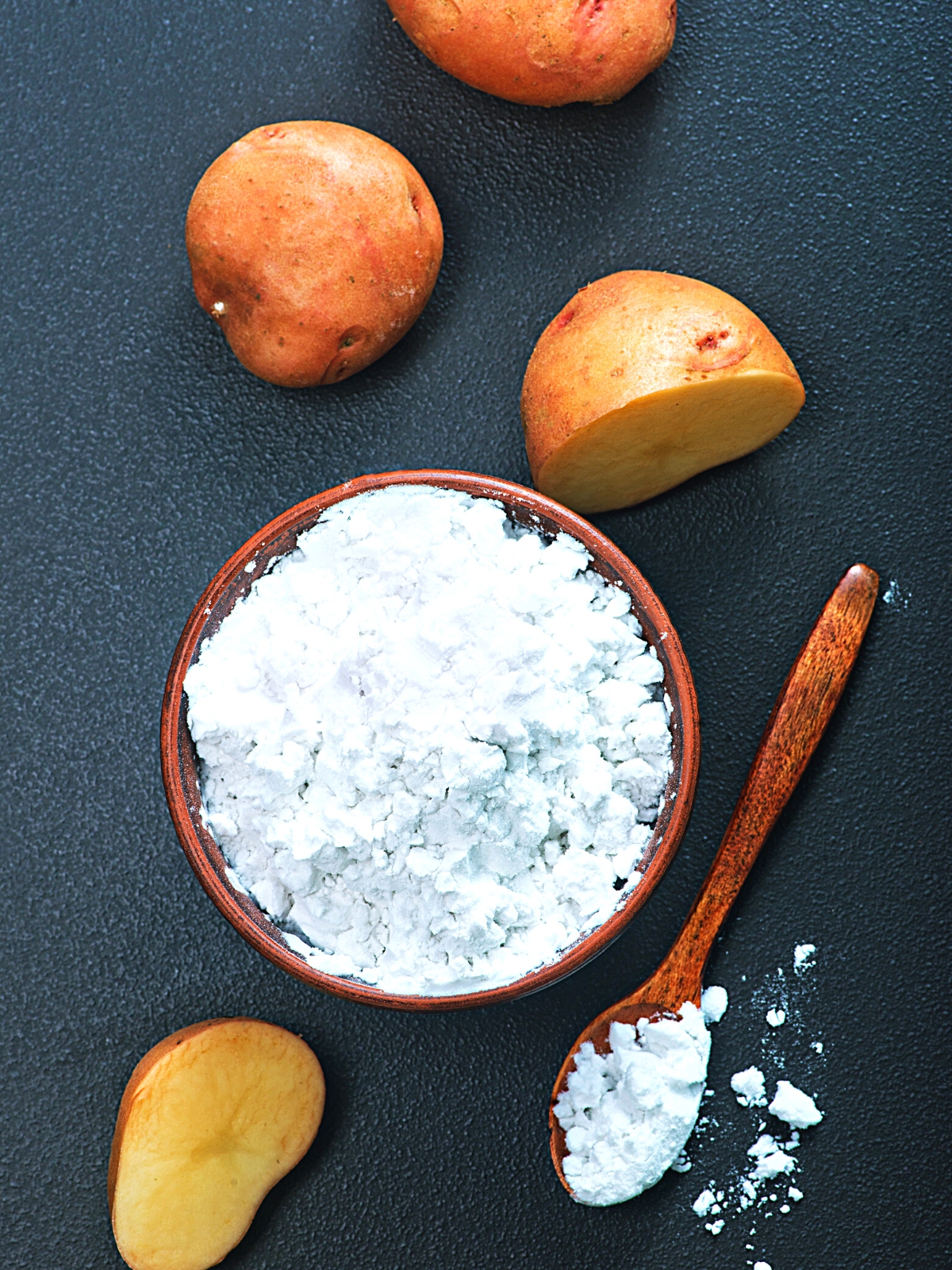 Potato Starch in a wooden bowl with raw potatoes on the side.