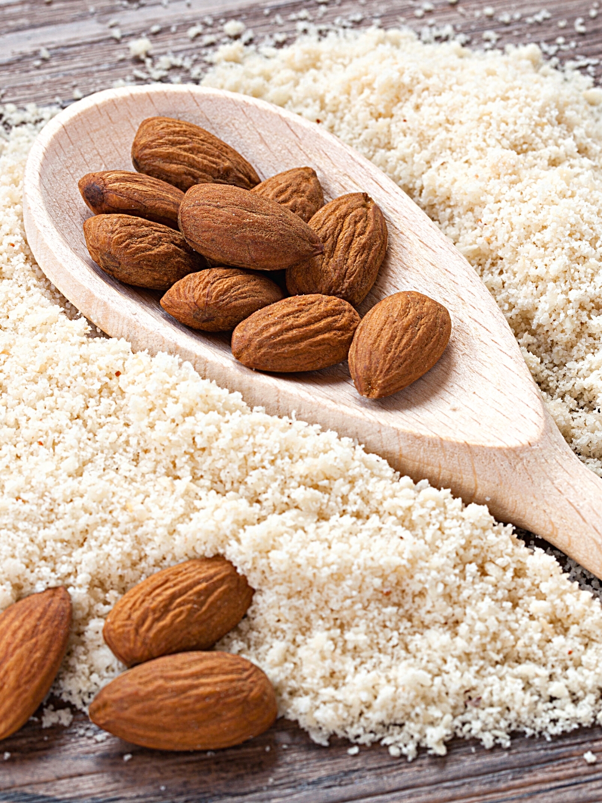 Almond Flour underneath wooden ladle with raw whole almonds.