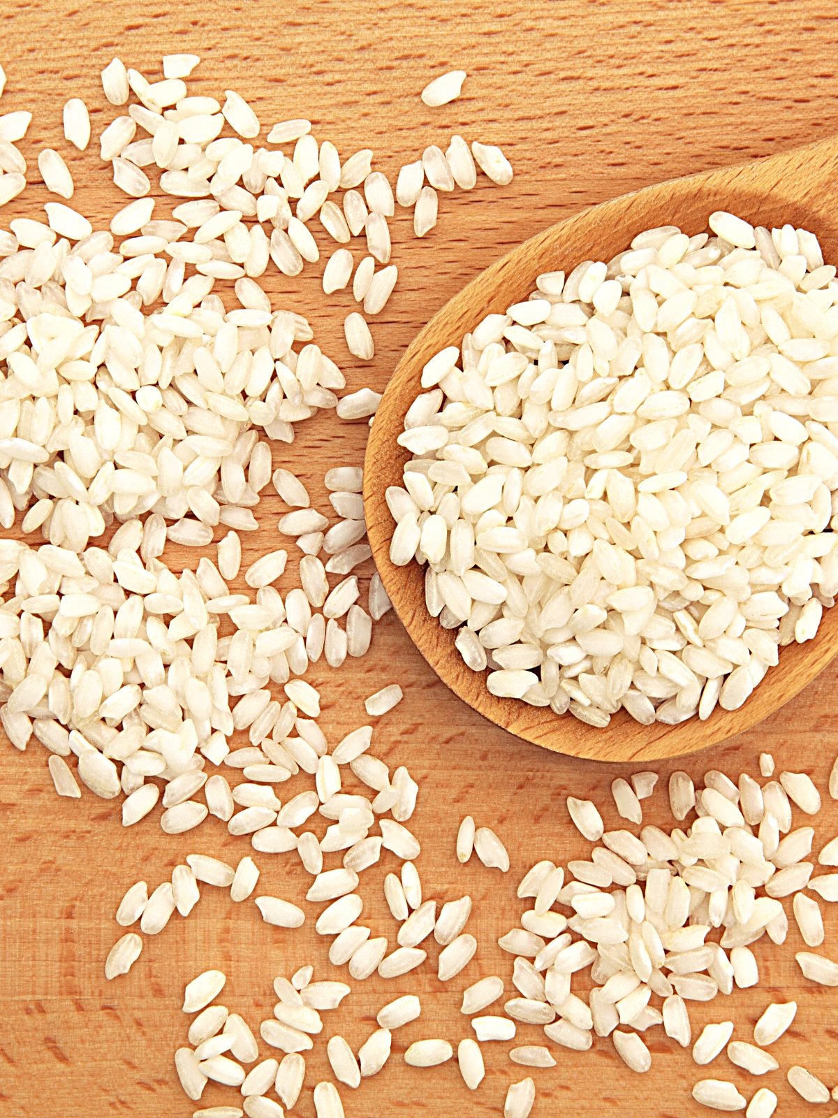 A wooden spoon of Carolina Gold Rice with a few rice scattered around.