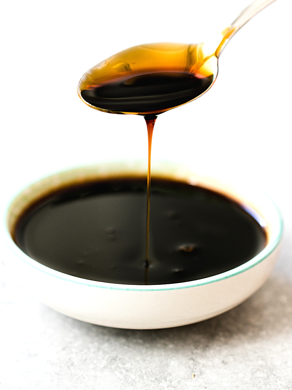 Organic Black Cane Sugar Molasses Dripping from Spoon into a white bowl.