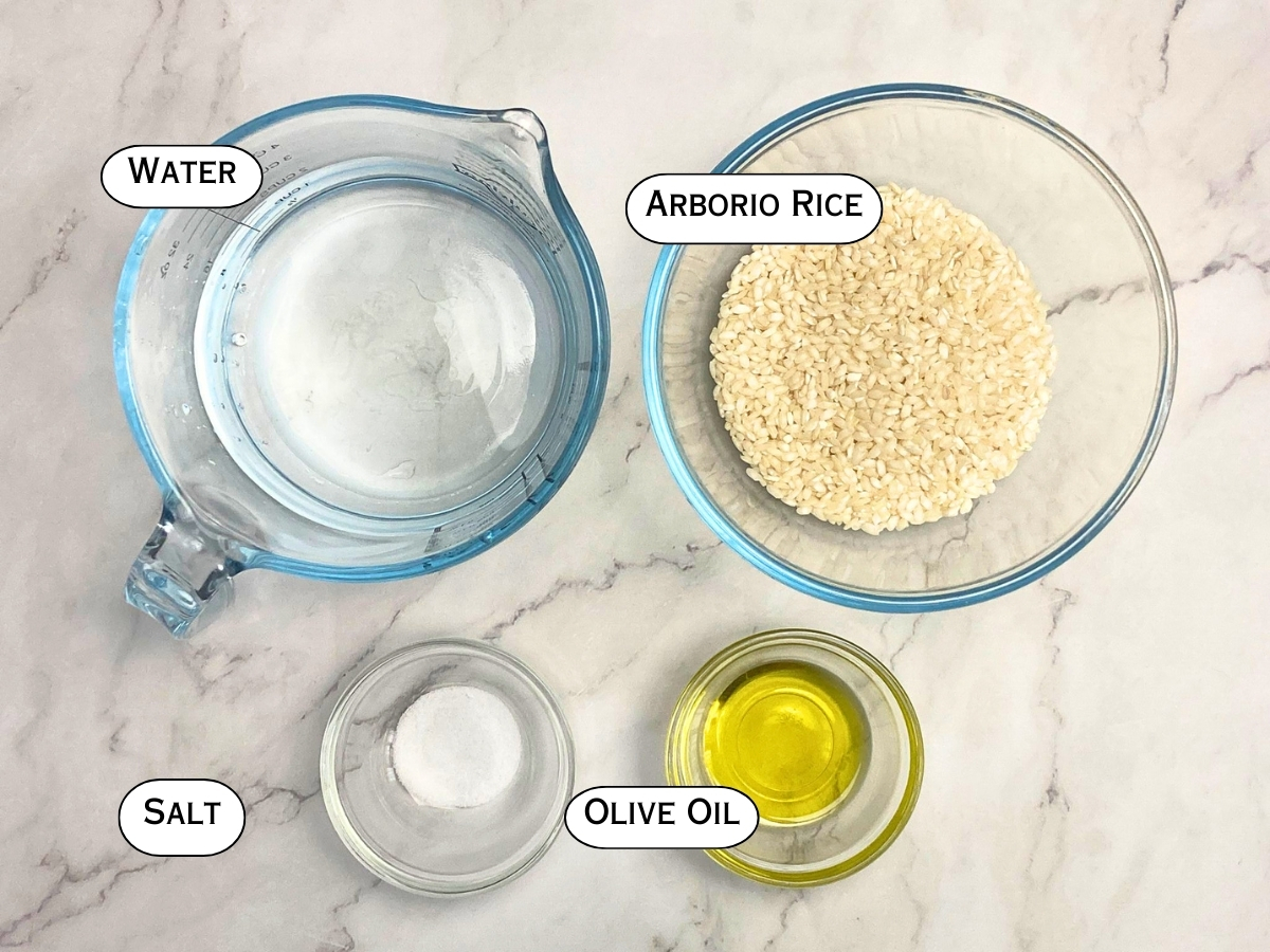 Ingredients needed to cook Arborio rice displayed on a marble countertop.