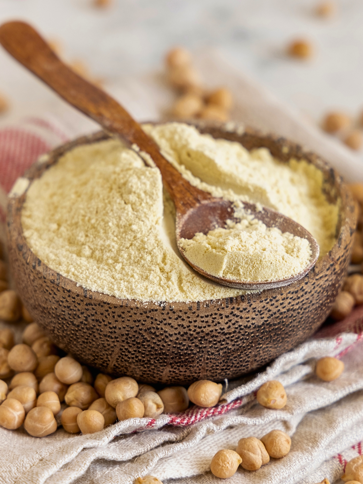 Chickpea Flour in a wooden bowl, with chickpeas scattered around.