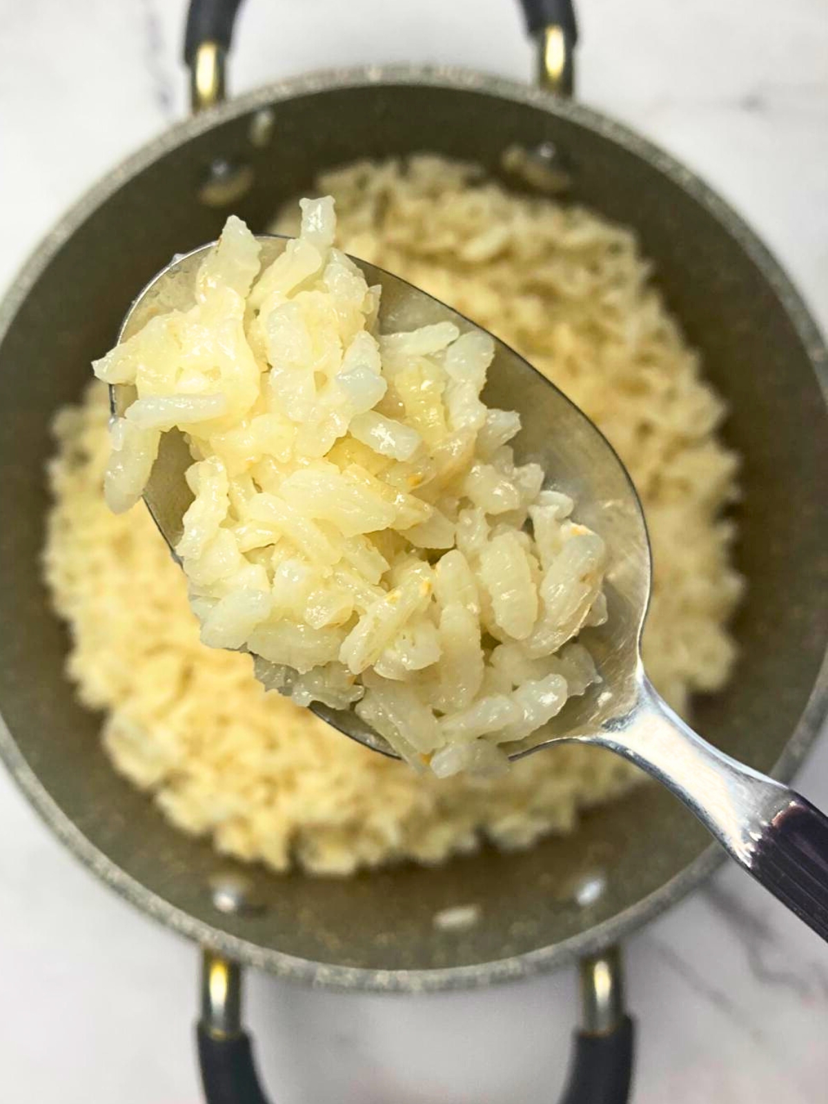 Spoon filled with rice lifting from saucepan.