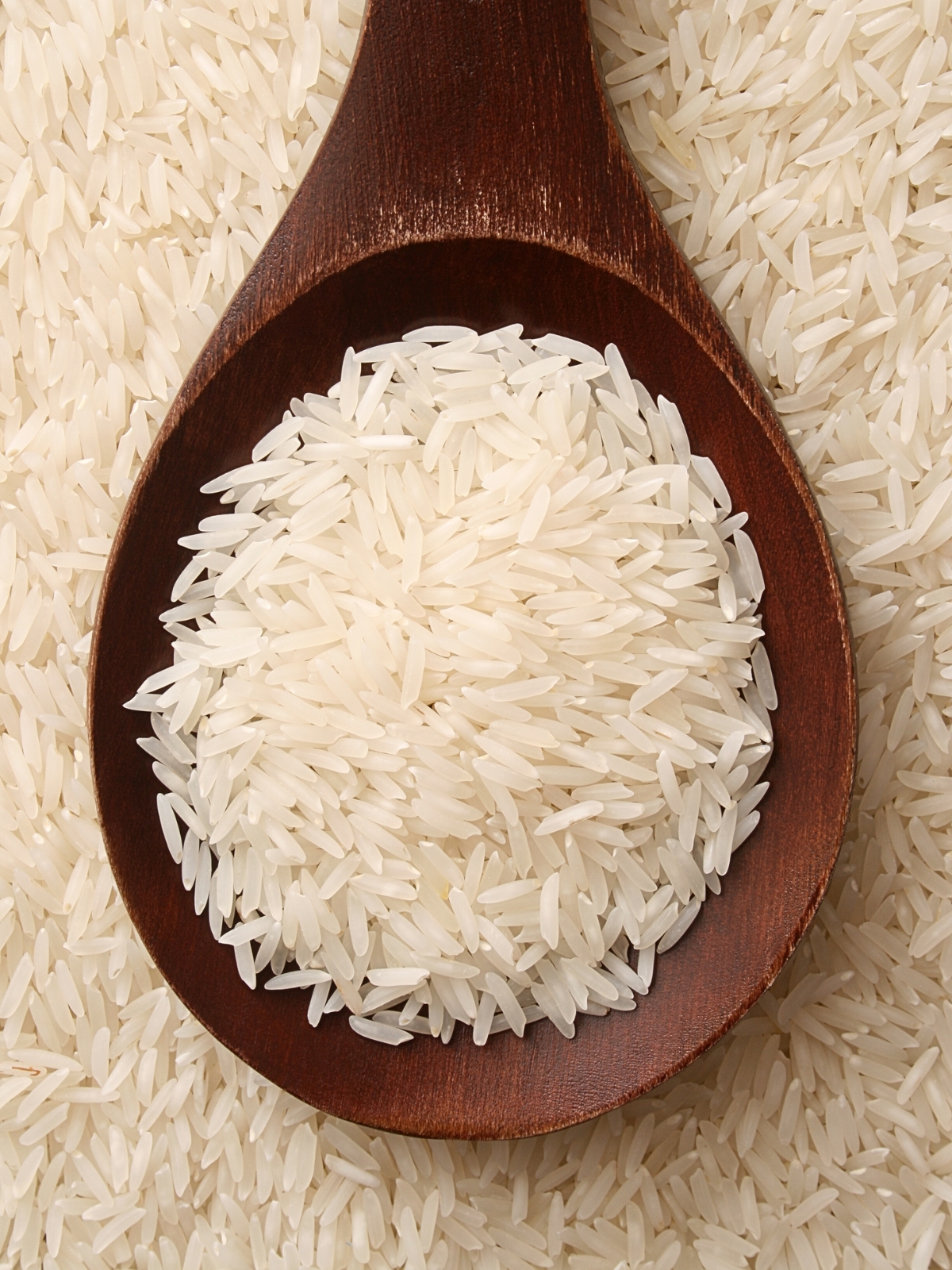 Basmati rice on a wooden ladle placed on a bed of raw basmati rice.