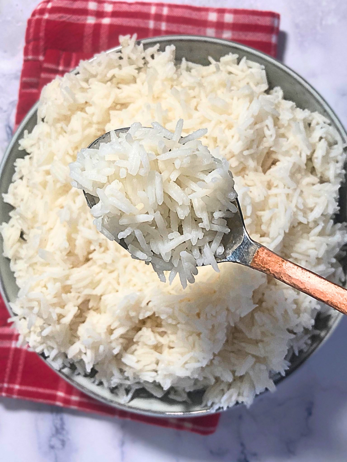 Spoon filled with cooked white basmati rice lifting from bowl.