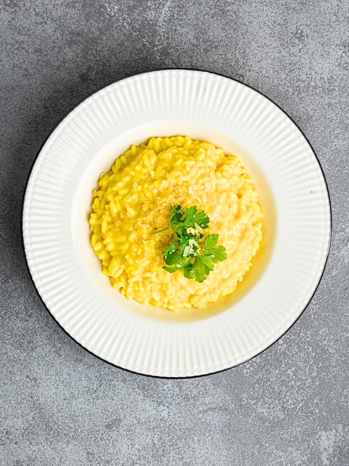 White plate filled with Risotto alla Milanese decorated with fresh parsley leaves.