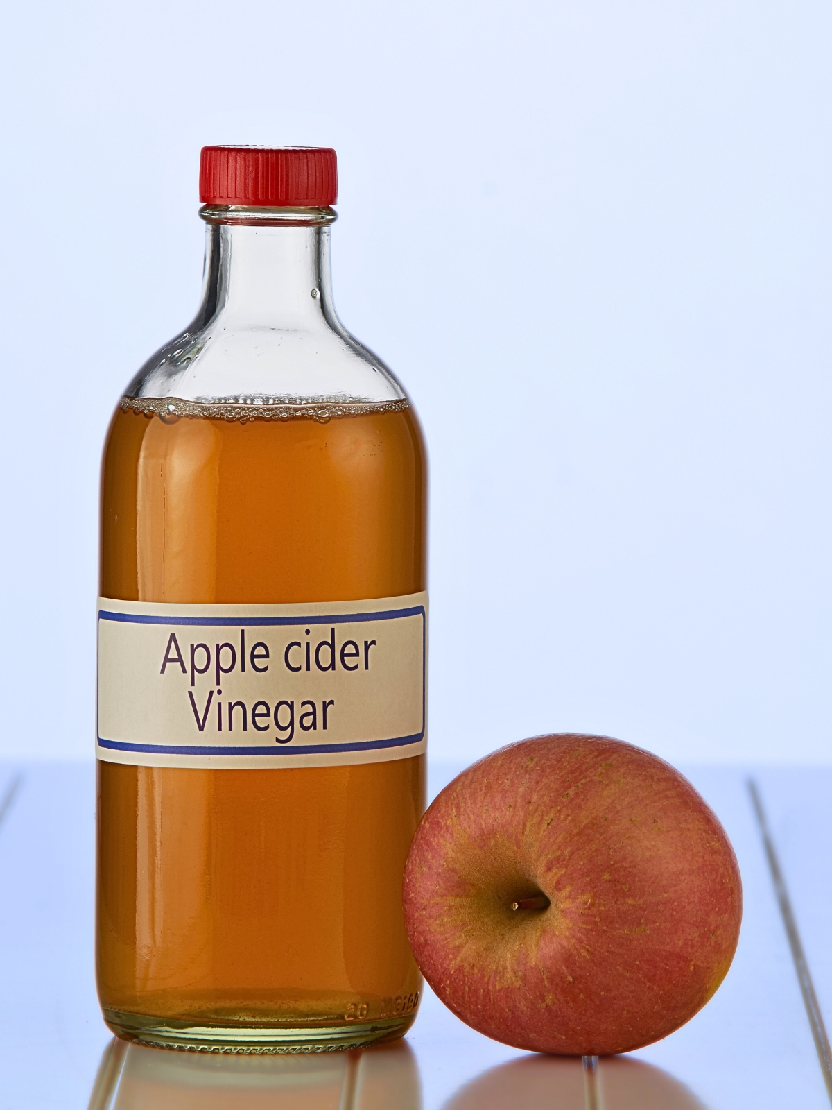 A bottle of apple cider vinegar with fresh apple on the side.