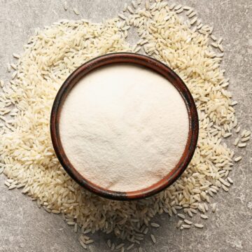 A bowl of rice flour with white rice grains around it.