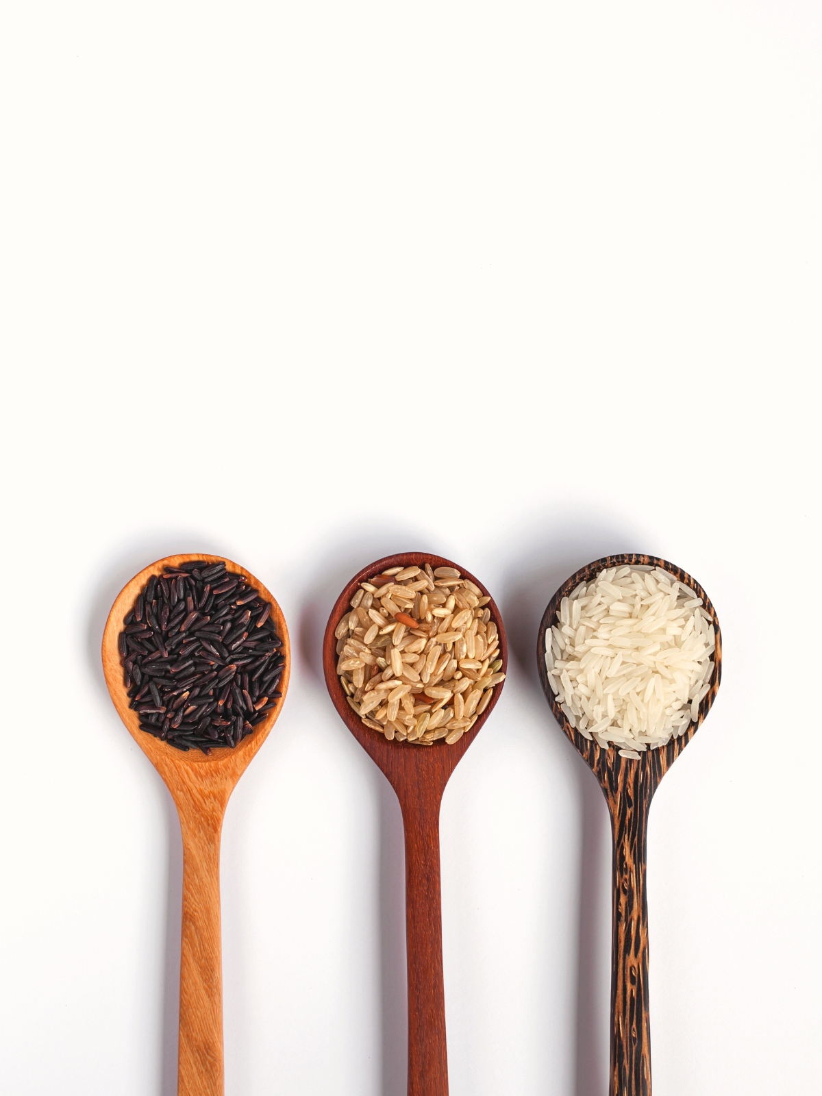 A wooden spoon with brown, white and black rice on a white background.