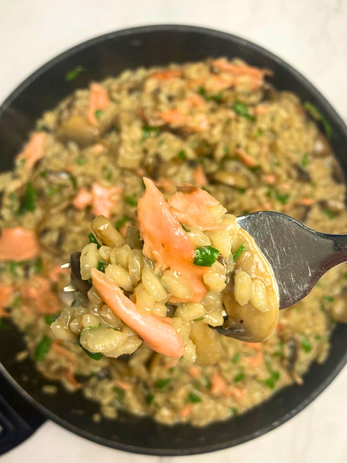 Salmon and mushroom risotto on a fork lifting from a frying pan.