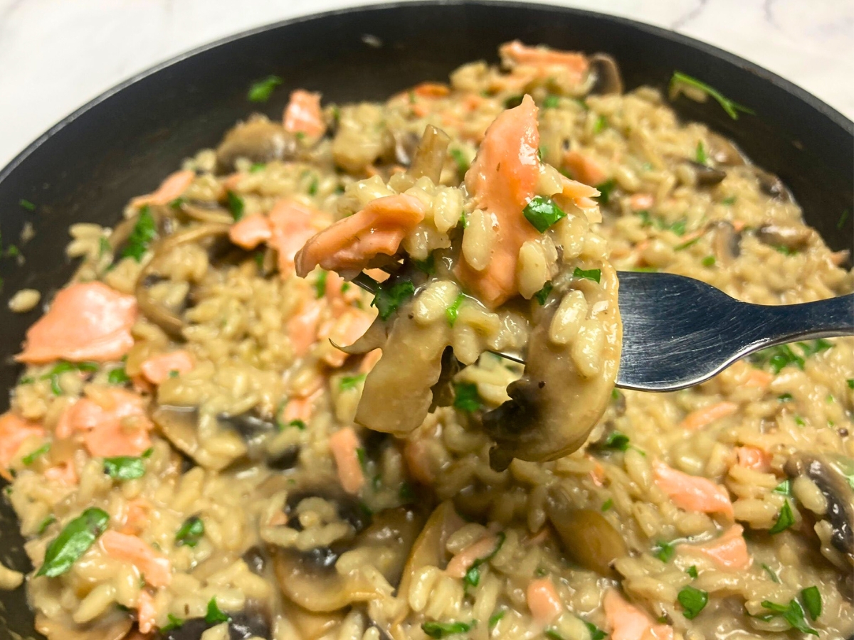 Salmon and mushroom risotto on a fork lifting from a frying pan.