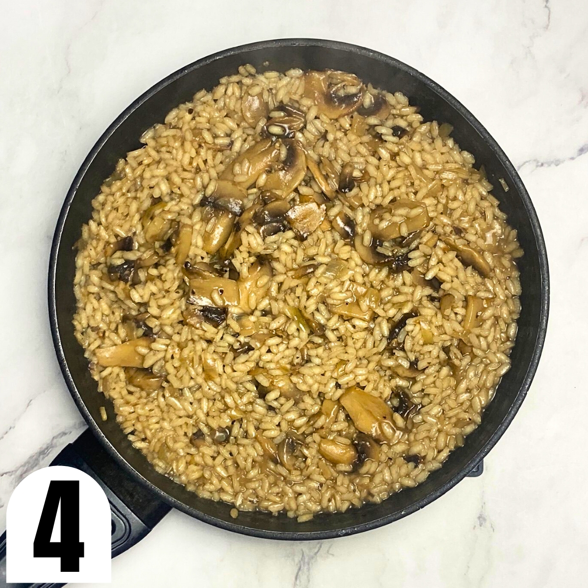 Mushroom risotto in saucepan on top of marble countertop.