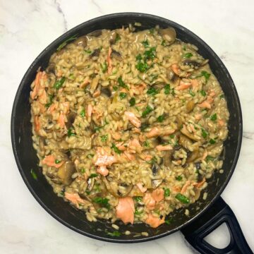 Salmon and mushroom risotto in saucepan on top of marble countertop.