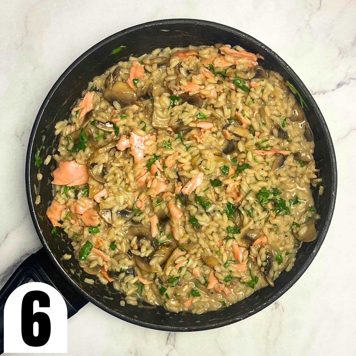 Salmon and mushroom risotto in saucepan on top of marble countertop.