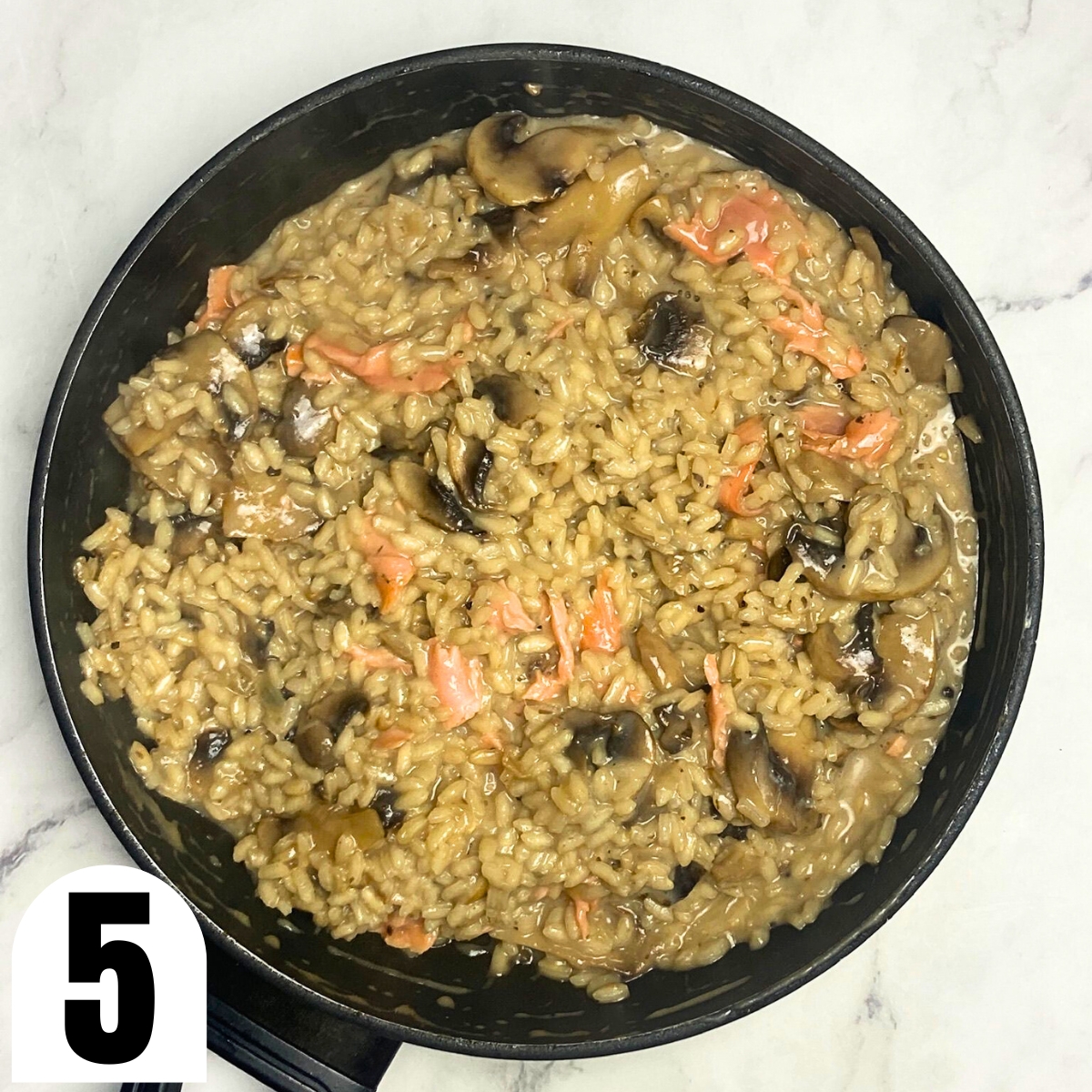 Salmon and mushroom risotto in saucepan on top of marble countertop.