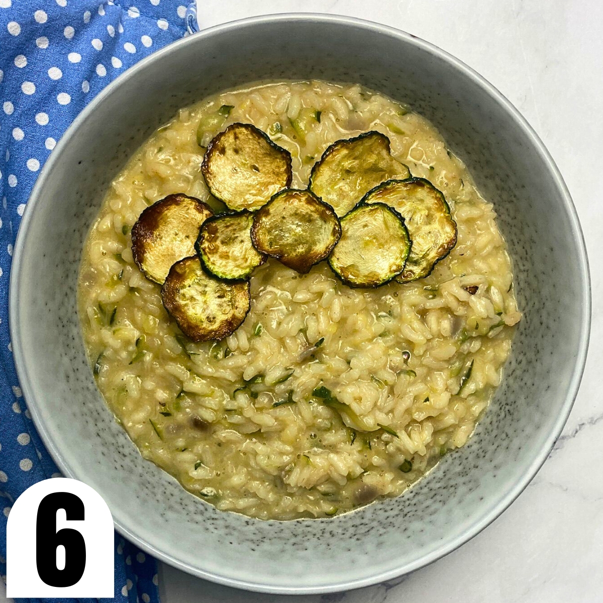 Grey plate with lemon zest and zucchini risotto with a blue tea towel.