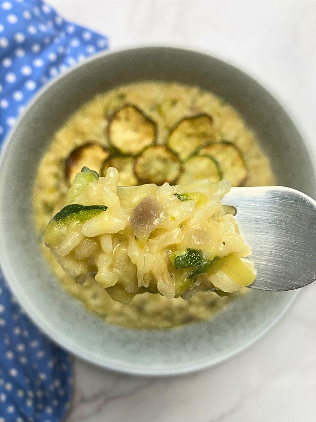 Lemon and zucchini risotto on a fork lifting from a plate.