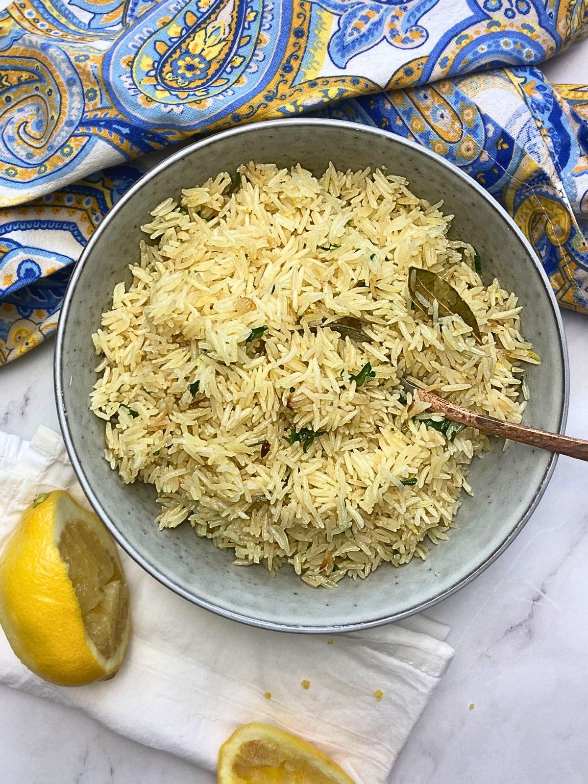 Lemon rice pilaf in a grey bowl with a copper spoon.