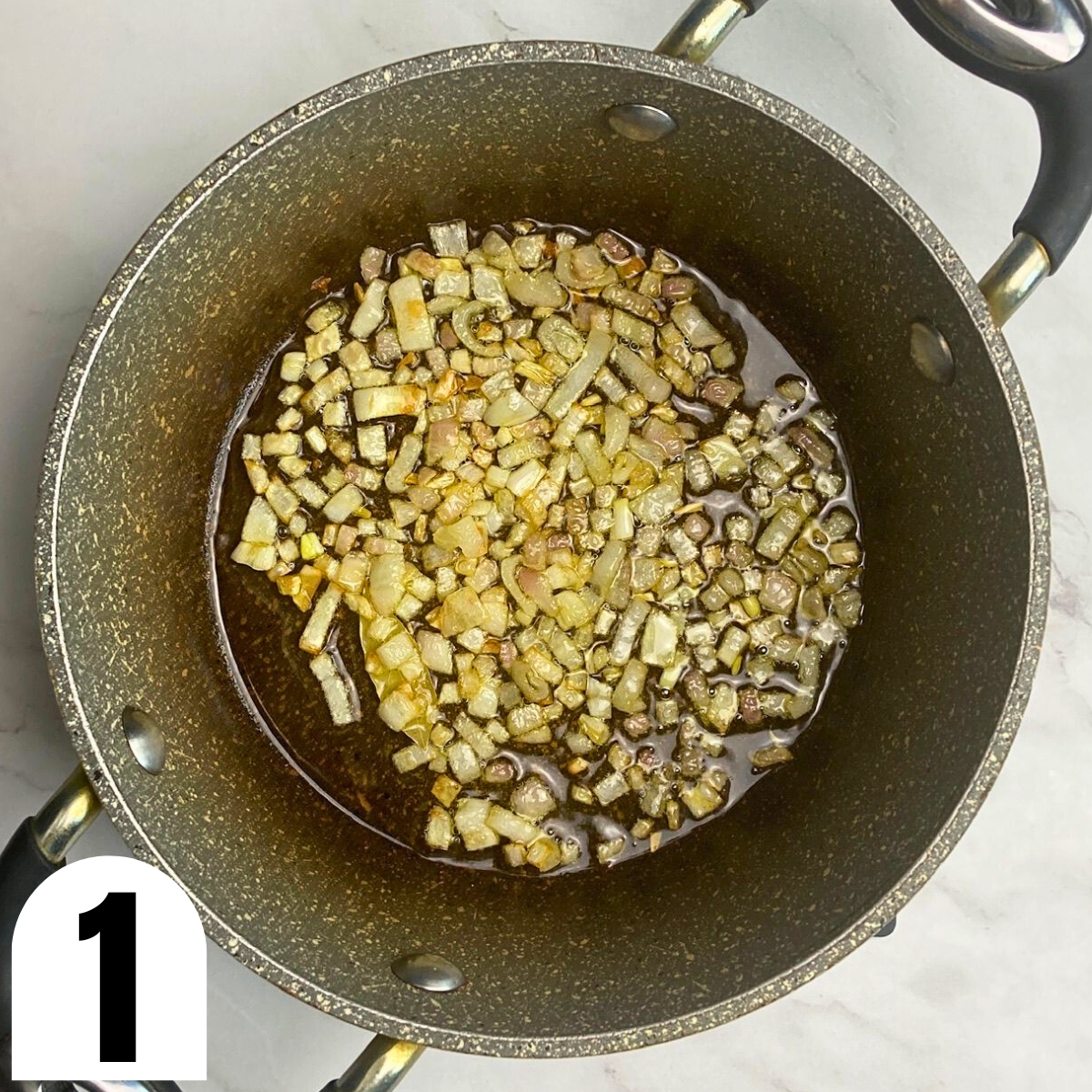 Onions sauteed in olive oil in grey saucepan.