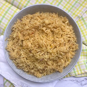 Bowl filled with saffron rice pilaf on top of a yellow and green tea towel.