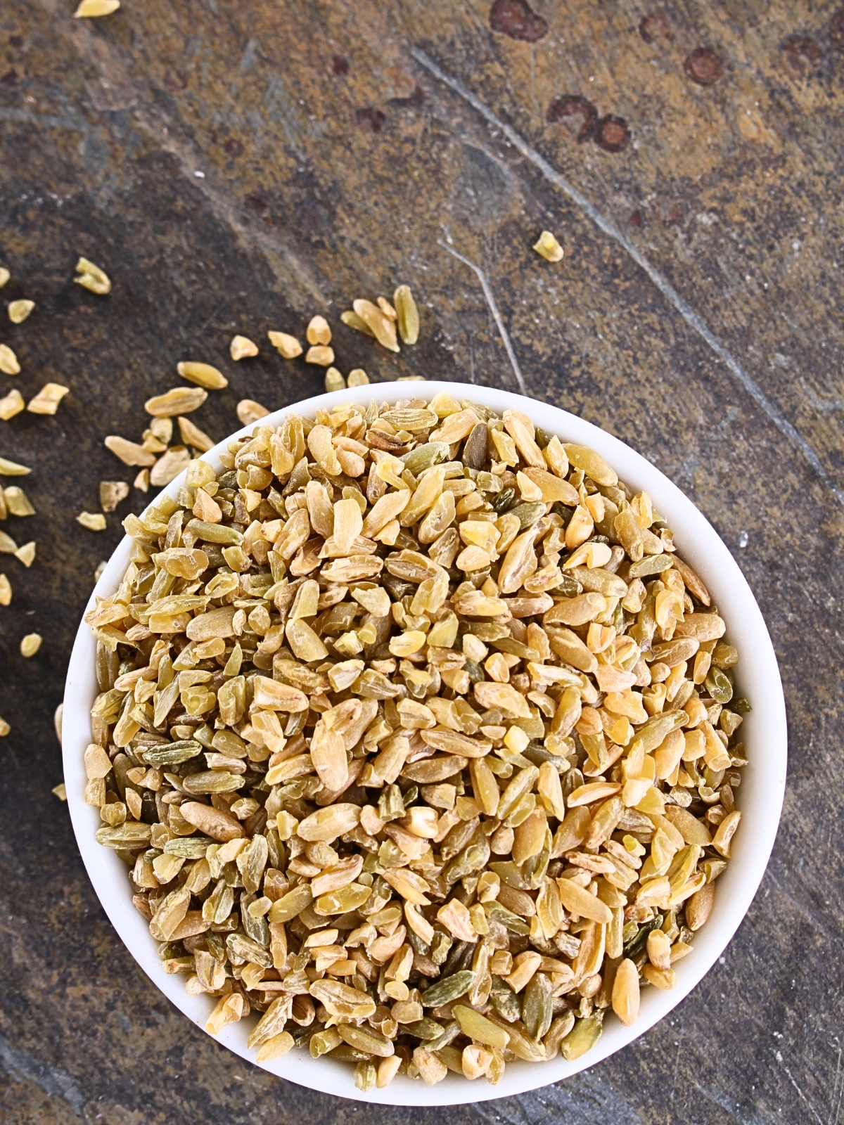 Uncooked Cracked Freekeh Grains in a white ceramic bowl.