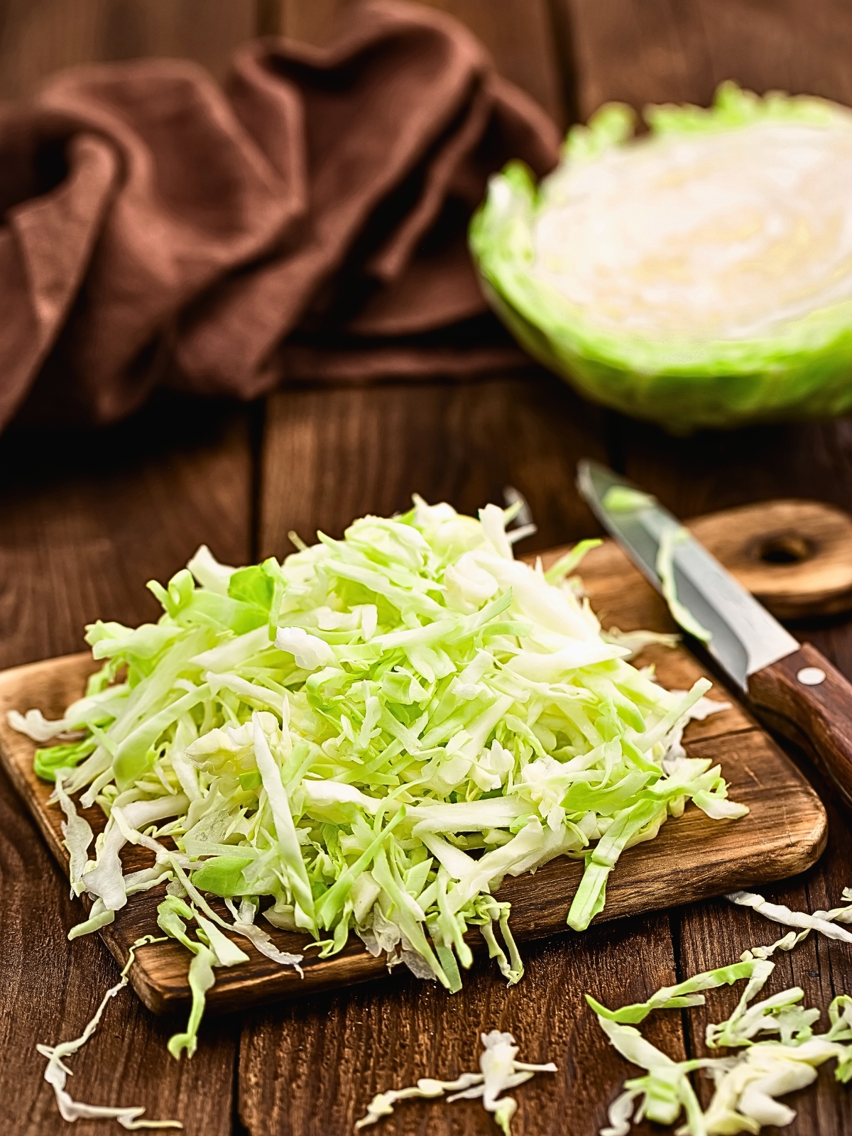 shredded cabbage on a wooden chopping board, with a knife on the side.