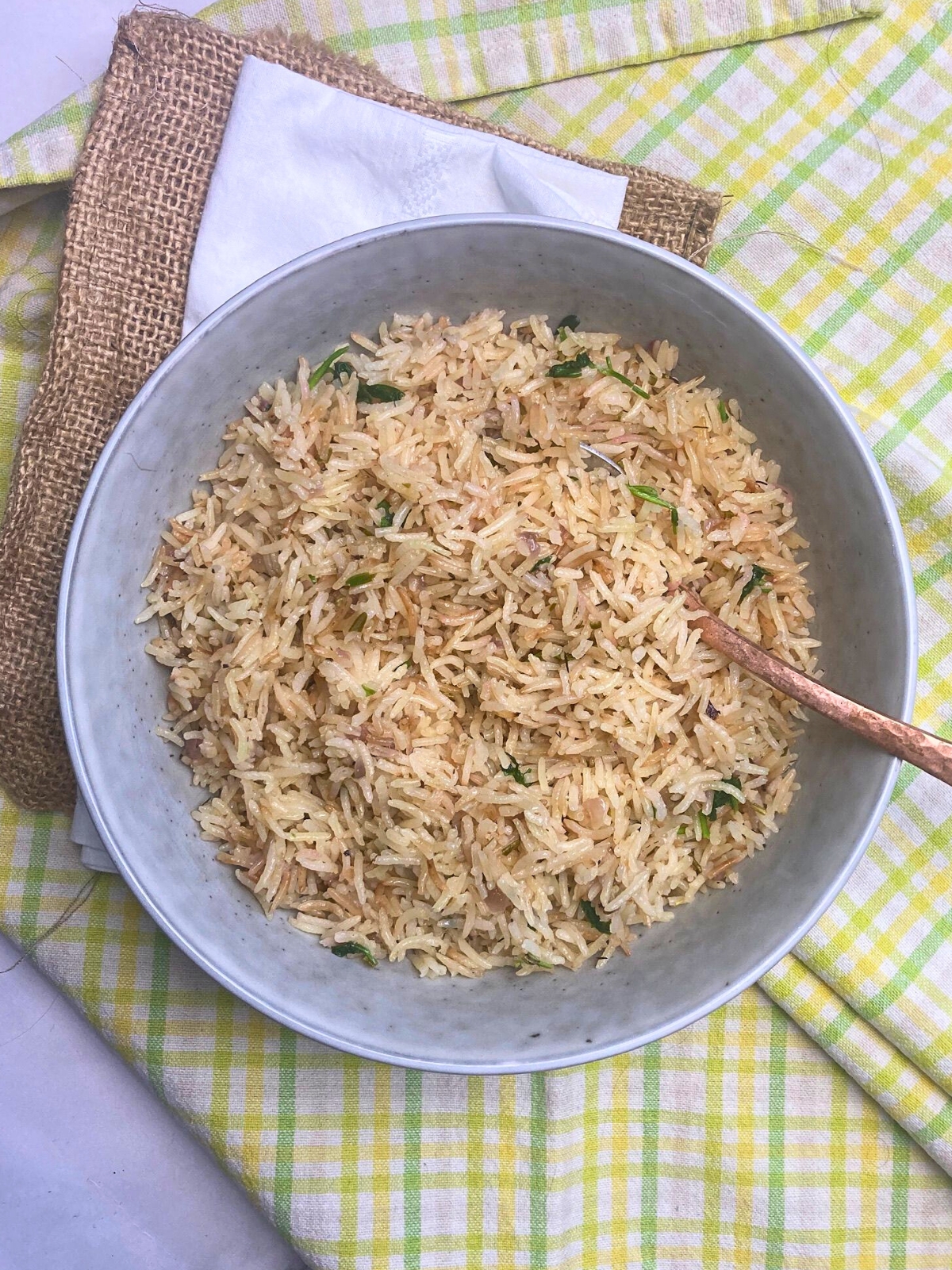 Pilaf rice with herbs in a grey bowl with a spoon in it.