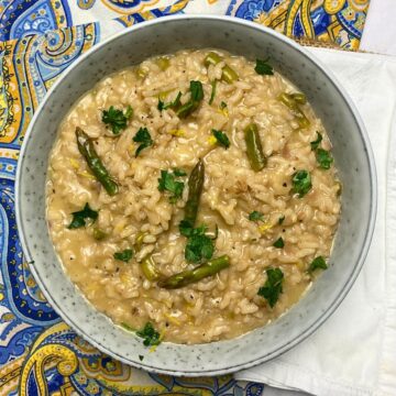 Grey bowl filled with asparagus risotto with chopped parsley and lemon zest on top.