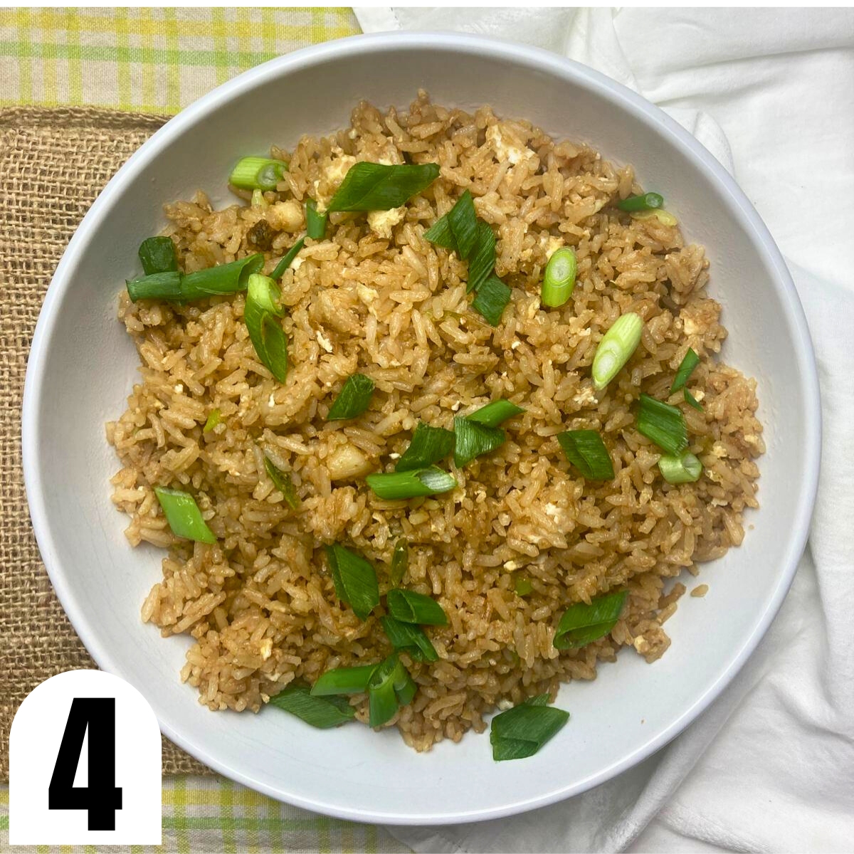 White bowl filled with fried rice with green onions and soy sauce.