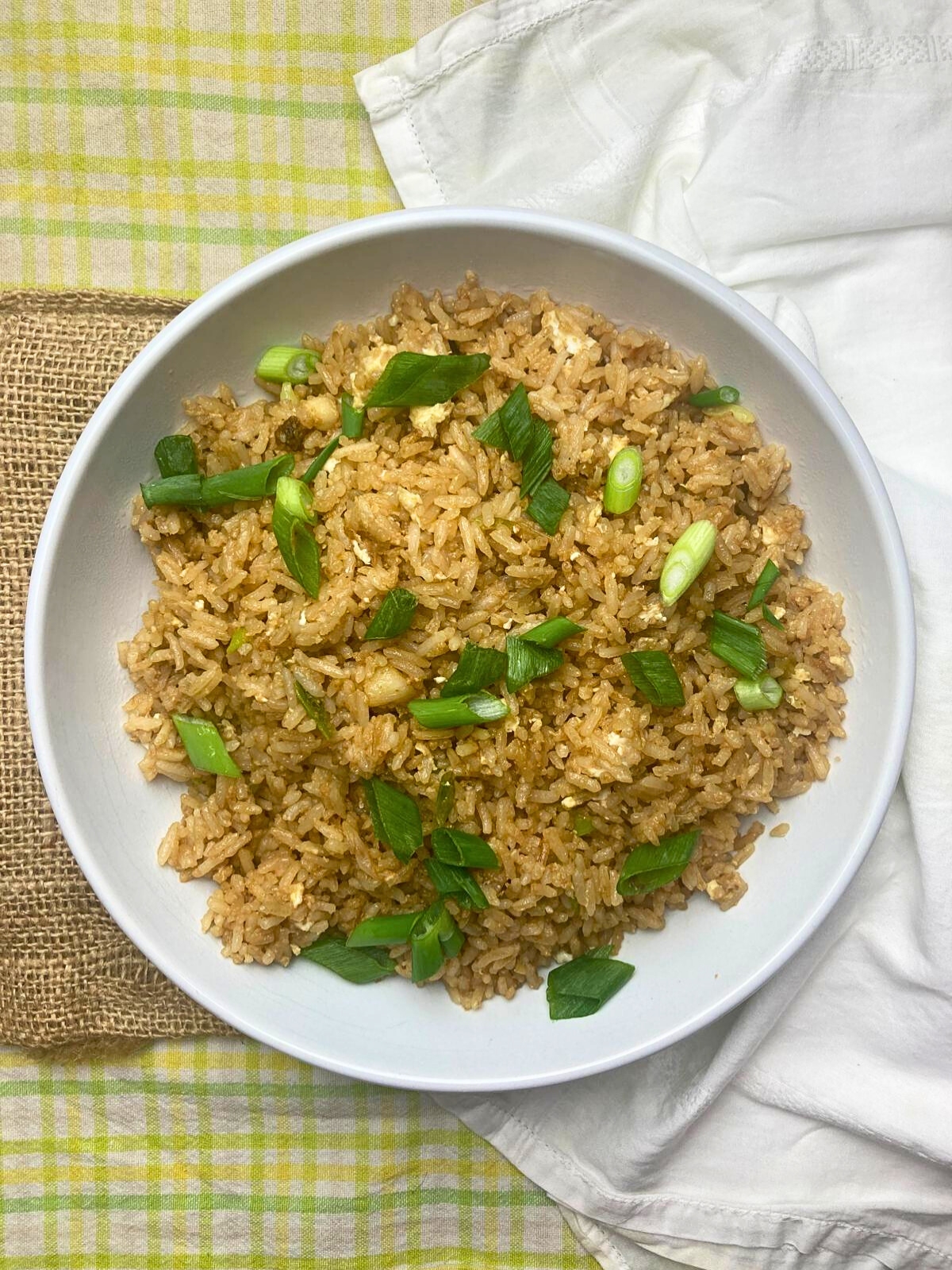 White bowl filled with garlic fried rice with green onion on top.