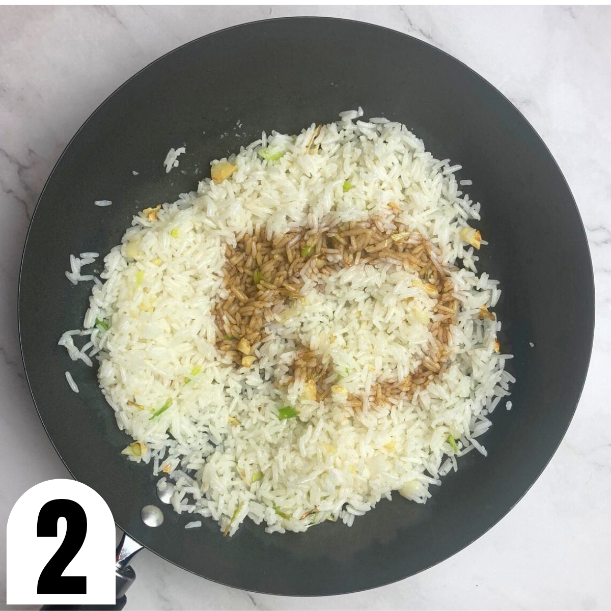 Wok with rice, garlic and green onion with soy sauce poured on top.