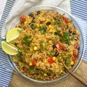 Glass plate filled with Mexican fried rice and two slices of lime on the side.