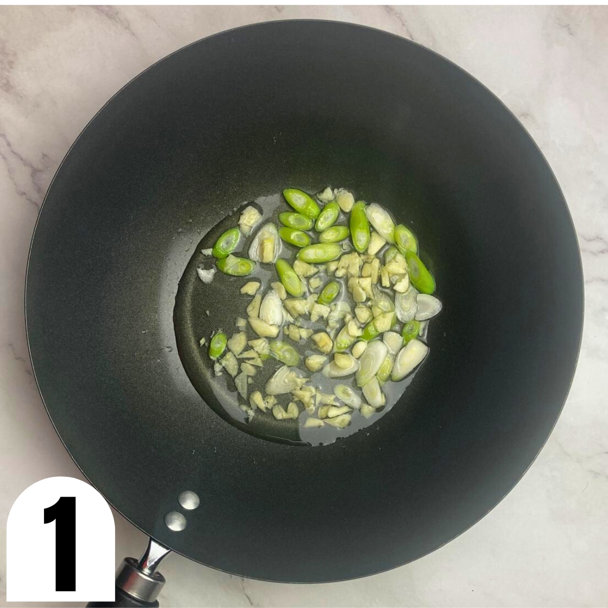 Wok with oil, green onion, and chopped garlic.