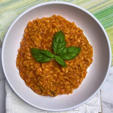 White bowl with tomato risotto in it, with fresh basil leaves on top.