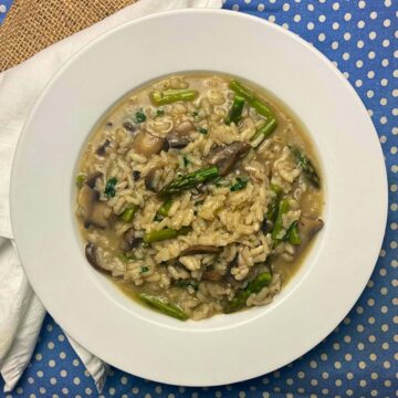 White plate with mushroom and asparagus risotto on top of a blue and white tea towel.