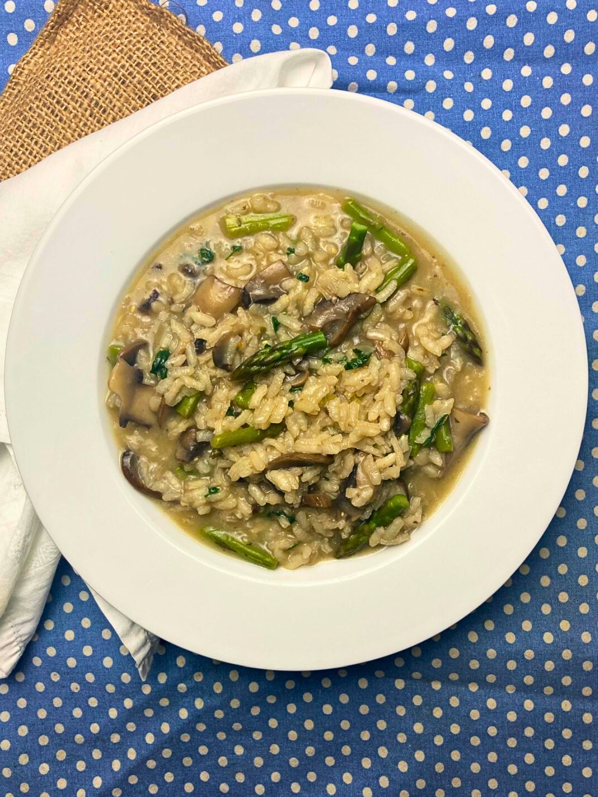 White plate with mushroom and asparagus risotto on top of a blue and white tea towel.