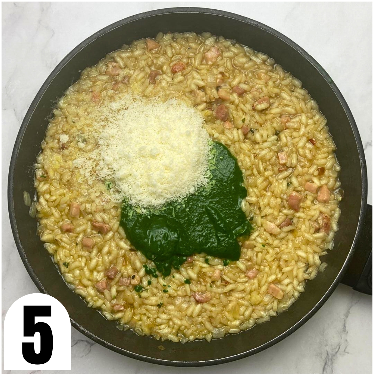 Frying pan with pancetta risotto with spinach puree and grated Parmesan cheese on top.