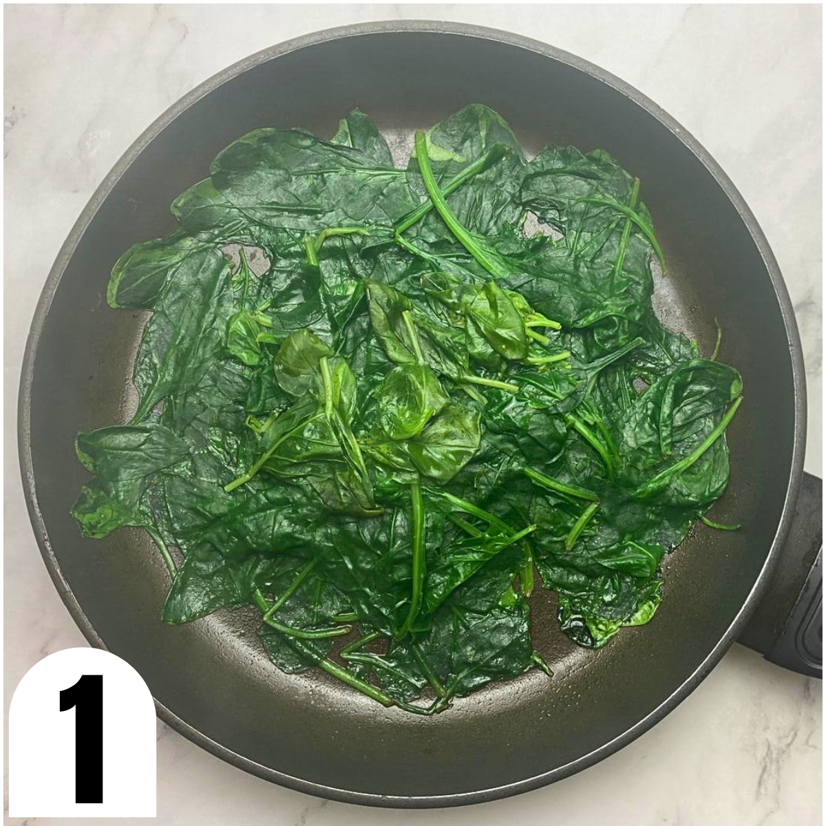 Frying pan with wilted spinach and basil leaves.