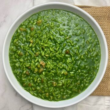 White bowl filled with spinach risotto and cubed pancetta.